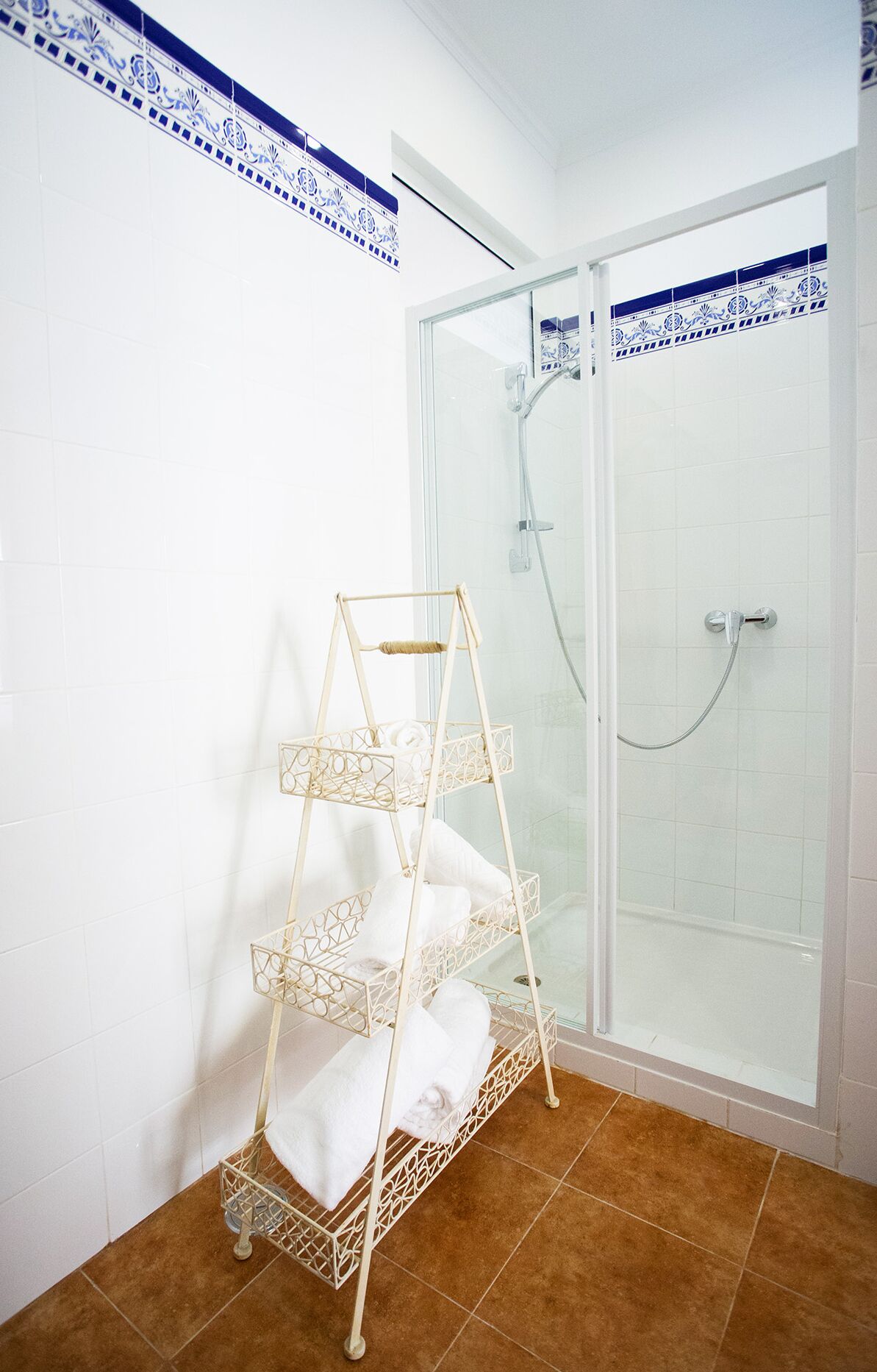 A bathroom with a glass shower enclosure, a white tiled wall, and a white towel rack with three shelves.