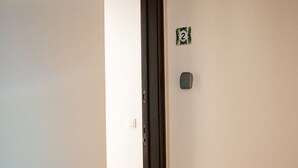 A hallway with a wooden parquet floor, a door with a dark frame, and a small green and white sign on the wall.