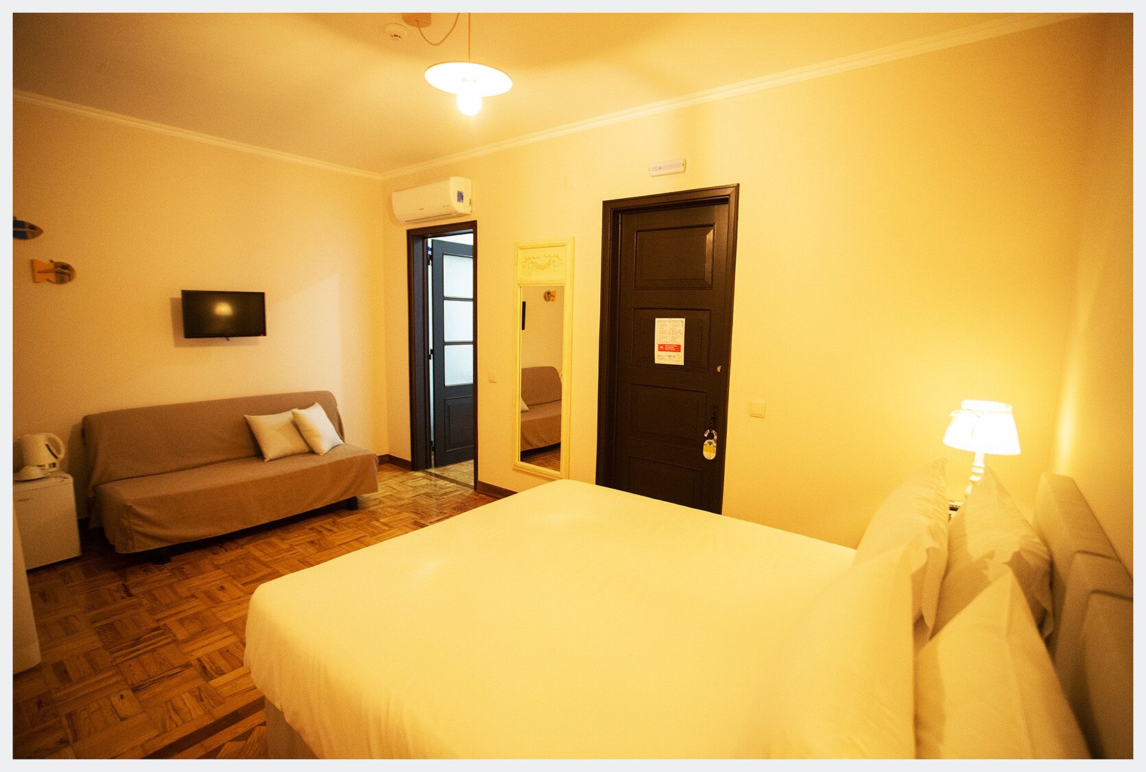 A hotel room with a bed, a sofa, a TV, and a door.