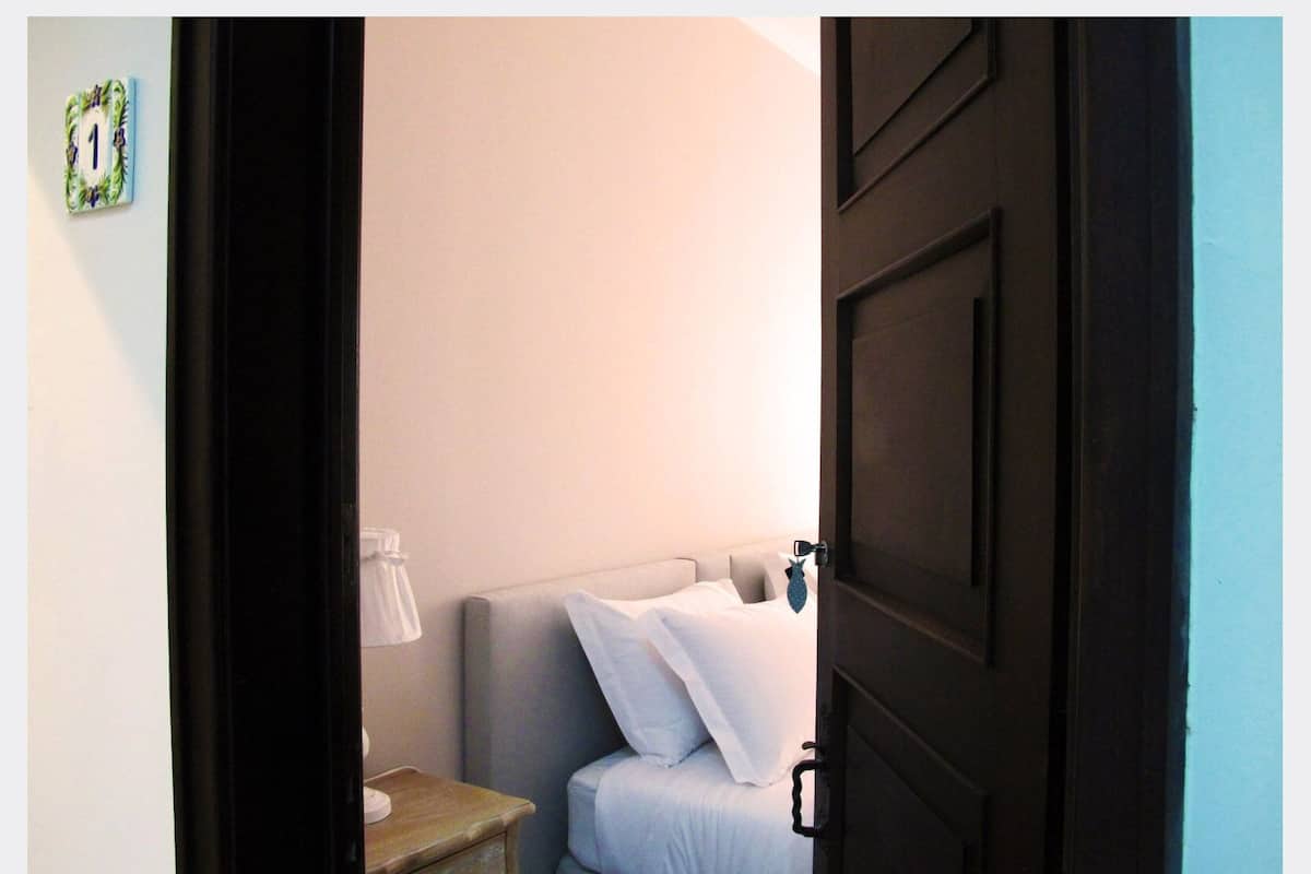 A bedroom with a bed, a nightstand, a lamp, and a door.