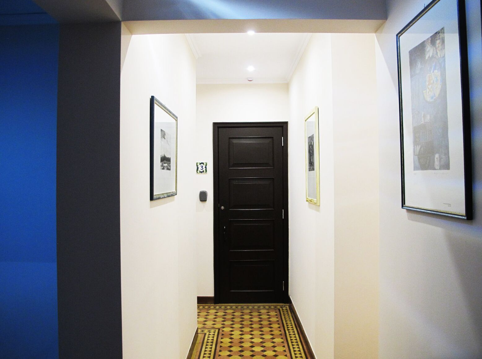 A hallway with a black door, framed pictures on the walls, and a patterned floor.