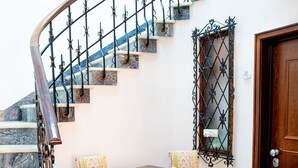A staircase with a wooden handrail and black metal balusters, leading to a landing with a marble floor and a wooden table with chairs.