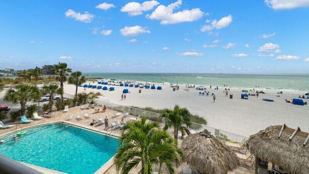 A beach view with a swimming pool, lounge chairs, and palm trees.