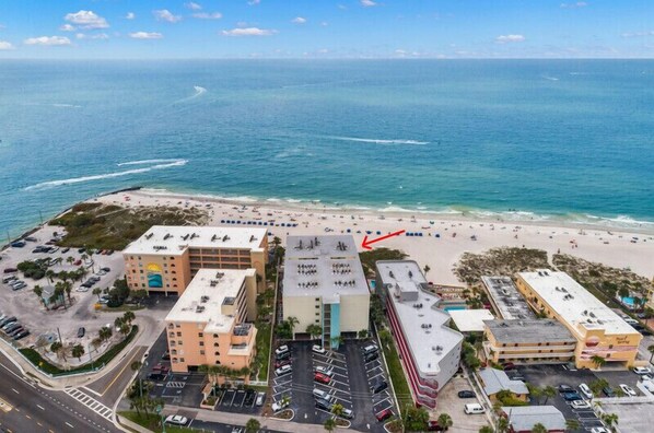 Luftaufnahme eines an der Küste gelegenen Hotels mit mehreren Gebäuden, einem Parkplatz und einem Strand.
