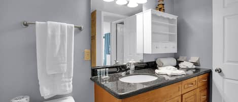 Un baño con inodoro blanco, lavamanos, armarios de madera y un espejo con iluminación.