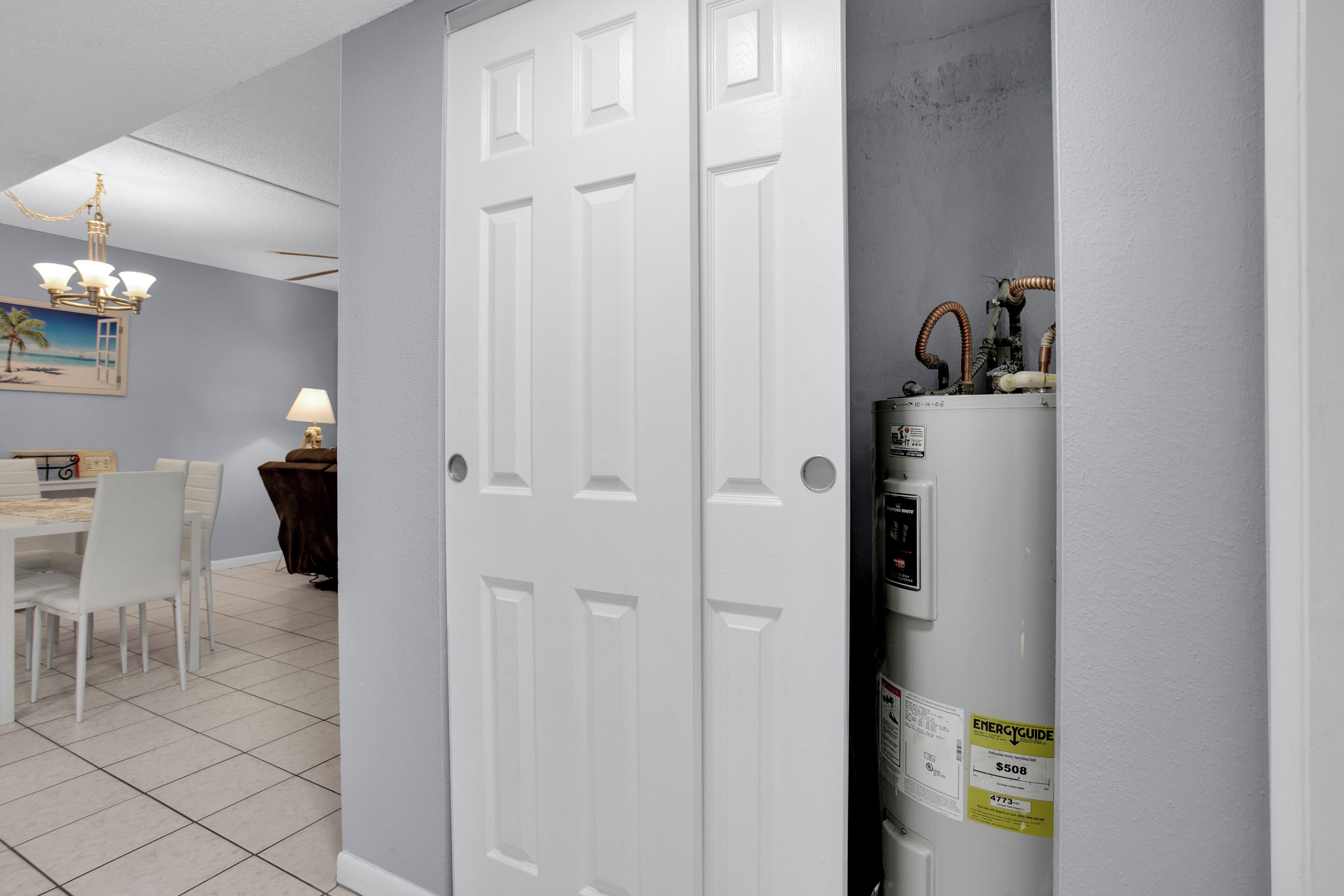 A room with a white door, a dining area with a table and chairs, and a wall-mounted heater.