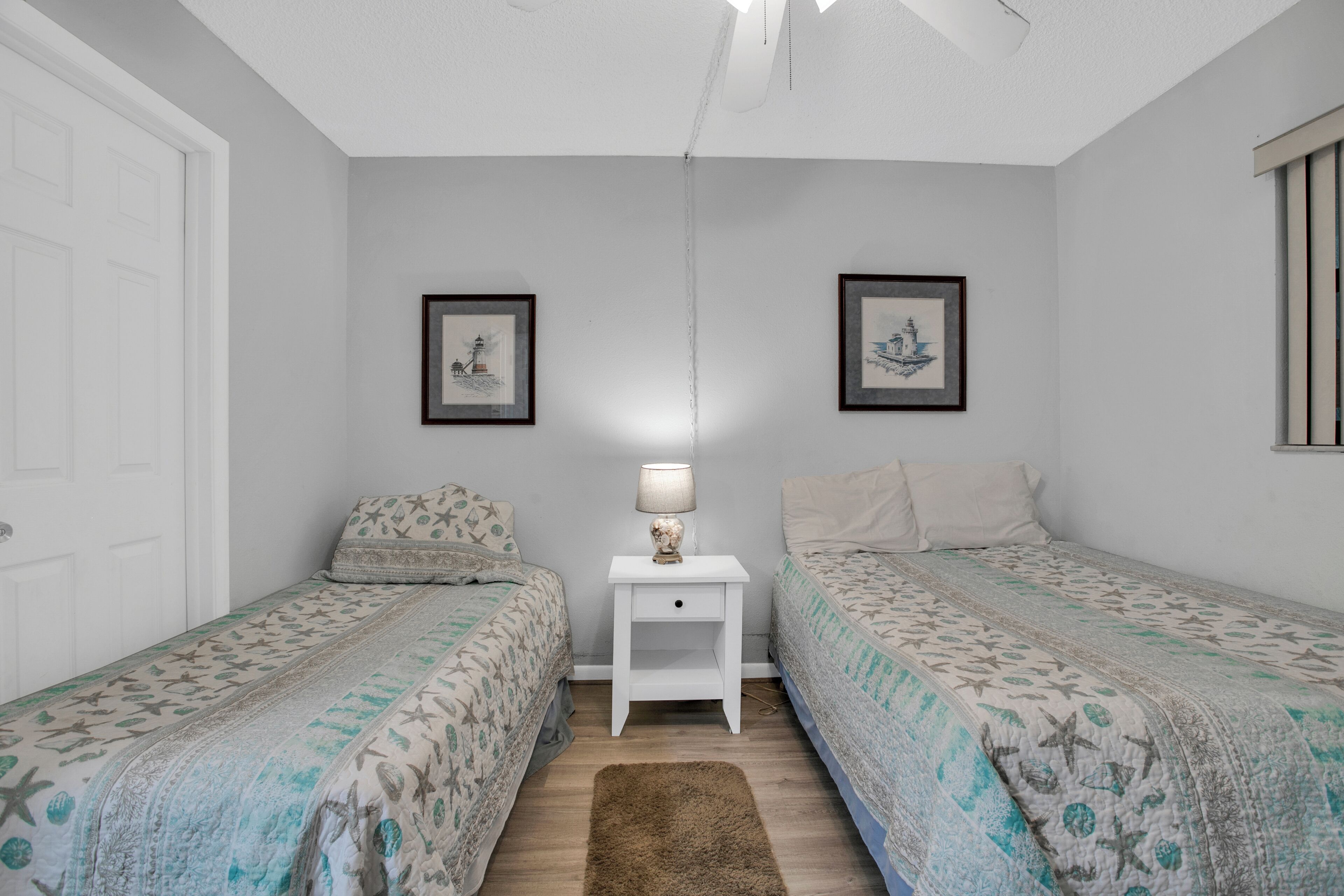 A bedroom with two single beds, a nightstand with a lamp, and two framed pictures on the wall.