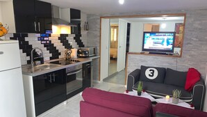 A modern kitchen with black and white tiles, a microwave, and a stove. There is a red sofa and a TV in the living area. - Cosy accommodation near Paris and Disneyland (Villiers-sur-Marne)