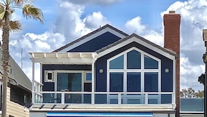 Una casa fronte mare su due piani con un balcone, ampie finestre e una zona piscina con lettini.