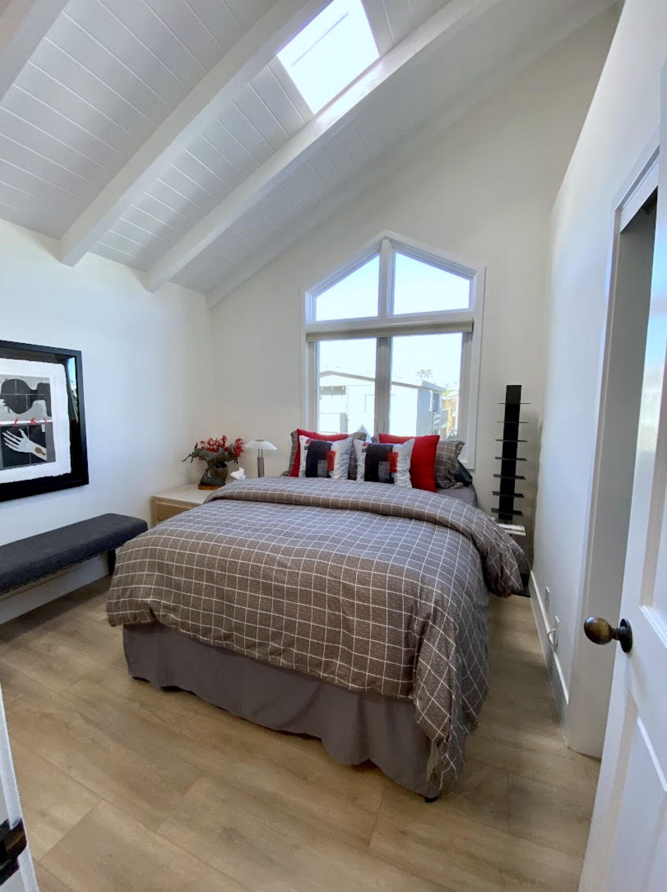 A bedroom with a large bed, a skylight, a window, and a bedside table with a lamp.