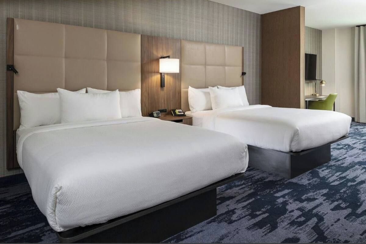 A hotel room with two beds, a desk, a chair, a TV, and a lamp.