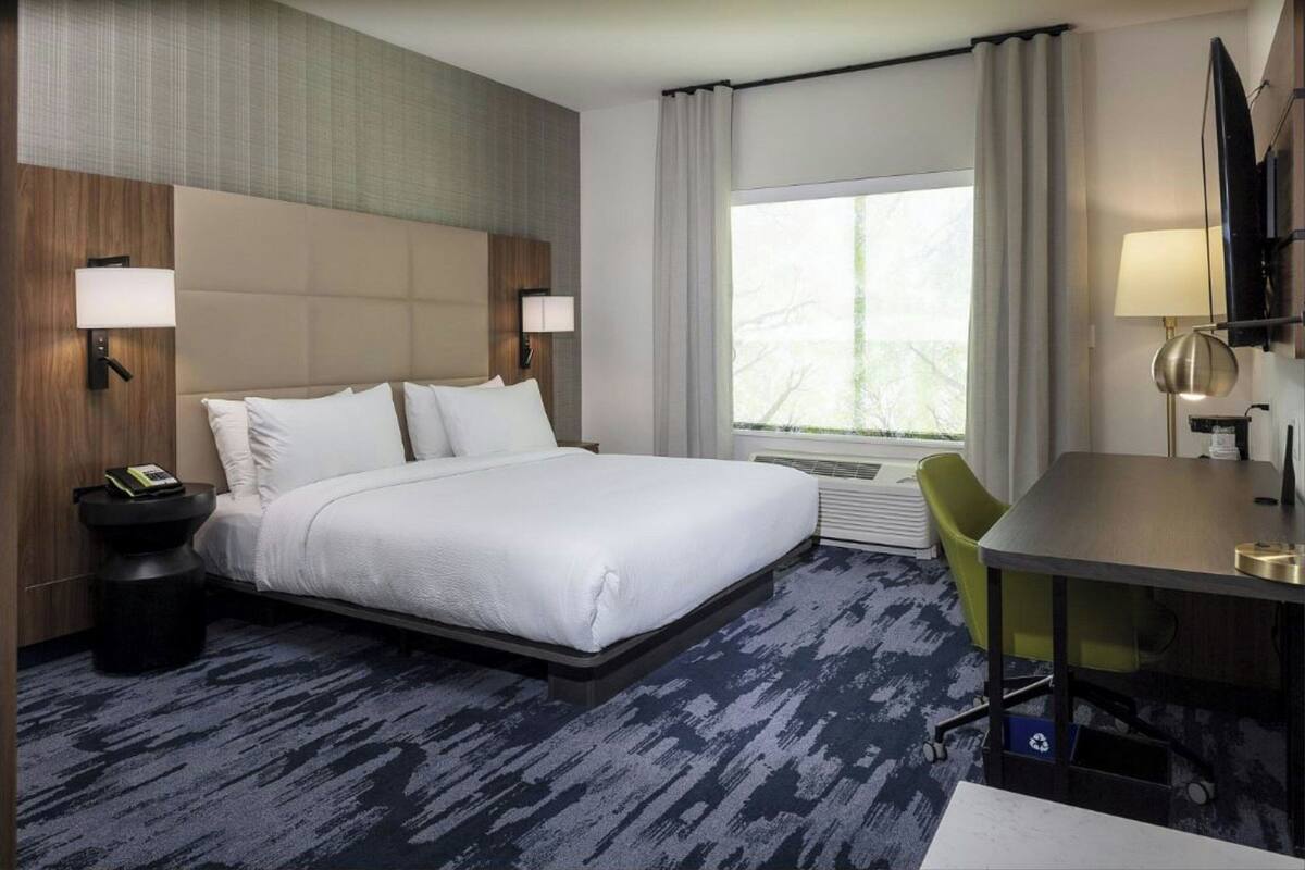 A hotel room with a large bed, a desk, a chair, a TV, and a window with curtains.