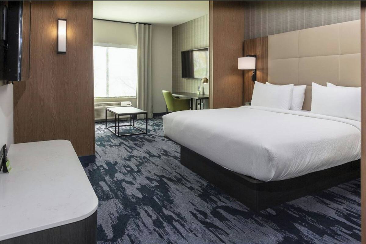 A hotel room with a large bed, a desk, a chair, a TV, and a window with curtains.