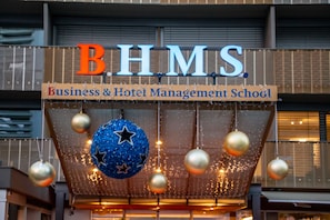 A sign for Business & Hotel Management School with a blue star ornament and hanging spherical decorations. - Über den Dächern von Luzern (Lucerne)