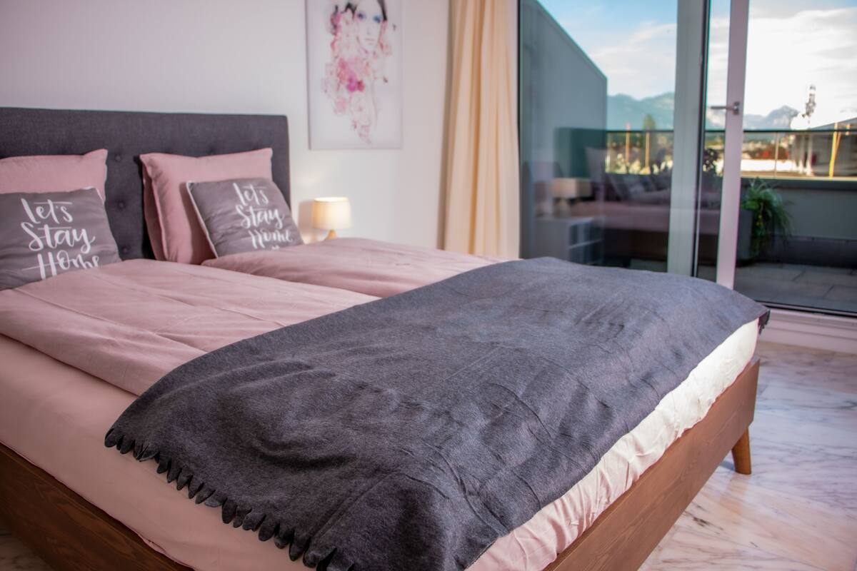 Un dormitorio con cama, almohadas y vistas a través de un ventanal.