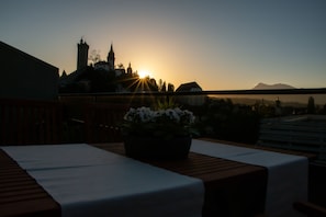 A terrace with a table and chairs, a potted plant, and a view of a distant mountain and buildings during sunset. - Über den Dächern von Luzern (Lucerne)