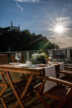 An outdoor dining area with a table set for two, overlooking a hill with a castle-like structure. - Über den Dächern von Luzern (Lucerne)