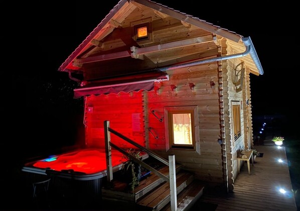 A wooden cabin with a red-lit exterior, a small porch, and a staircase leading to the entrance.