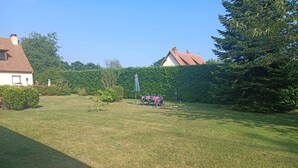A grassy backyard with a patio table and chairs, surrounded by hedges and trees.