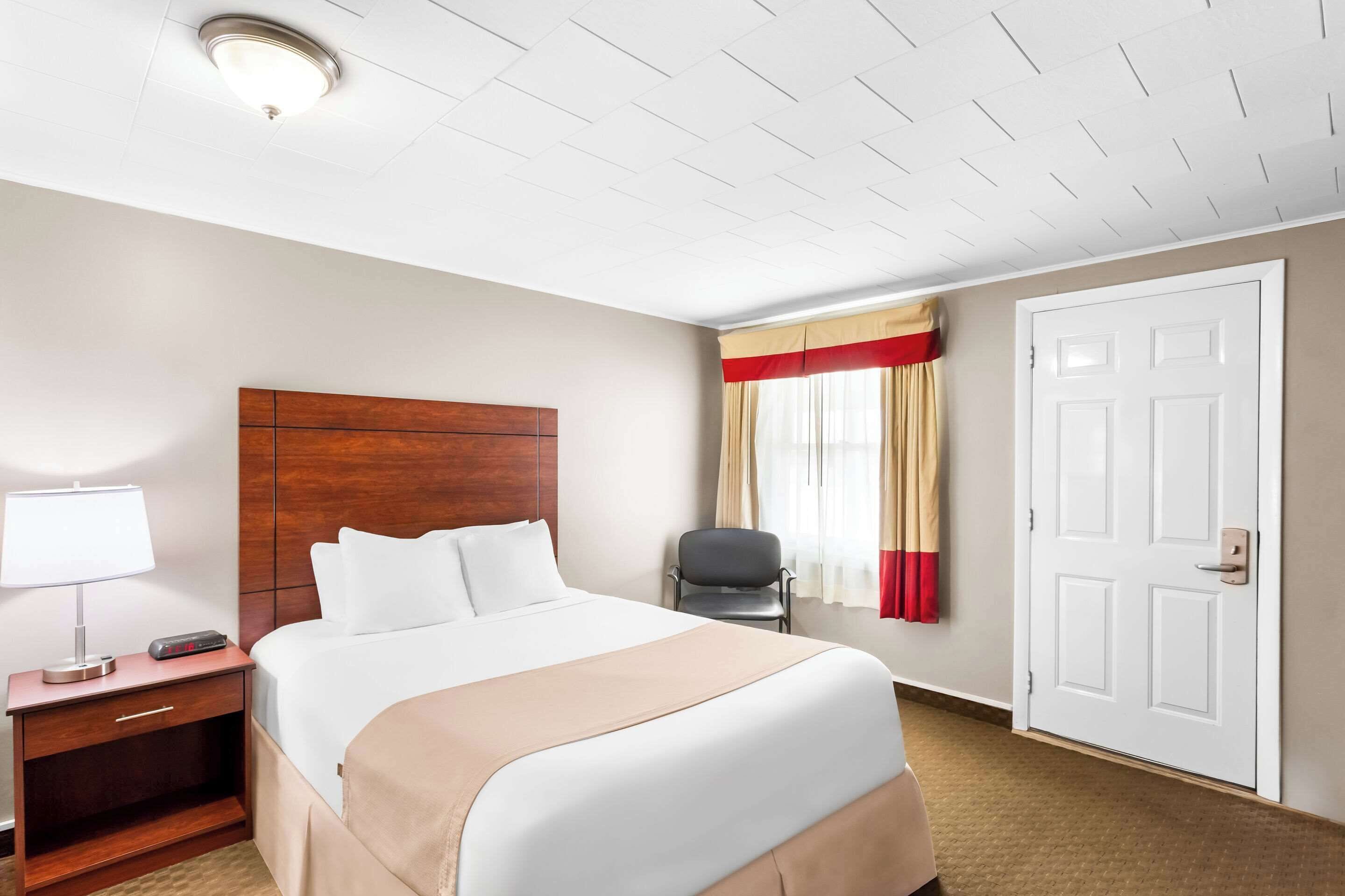 Una camera d'albergo con un letto grande, un comodino con una lampada, una sedia e una porta.