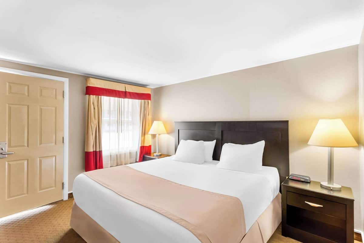 A hotel room with a large bed, two bedside tables with lamps, a door, and a window with curtains.