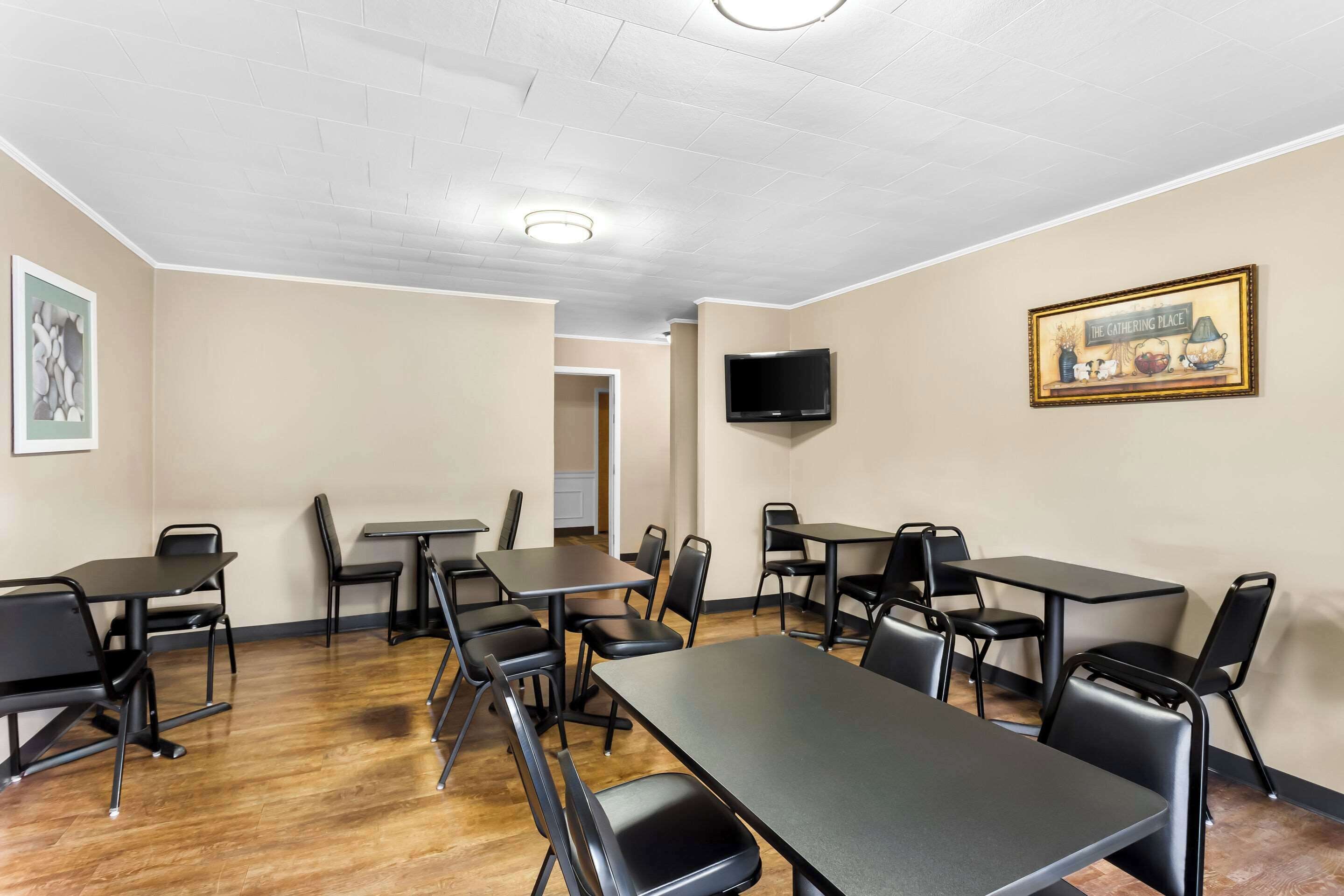 Une salle de conférence équipée de plusieurs tables et chaises, d’un téléviseur à écran plat fixé au mur et d’un tableau encadré placé au-dessus du téléviseur.