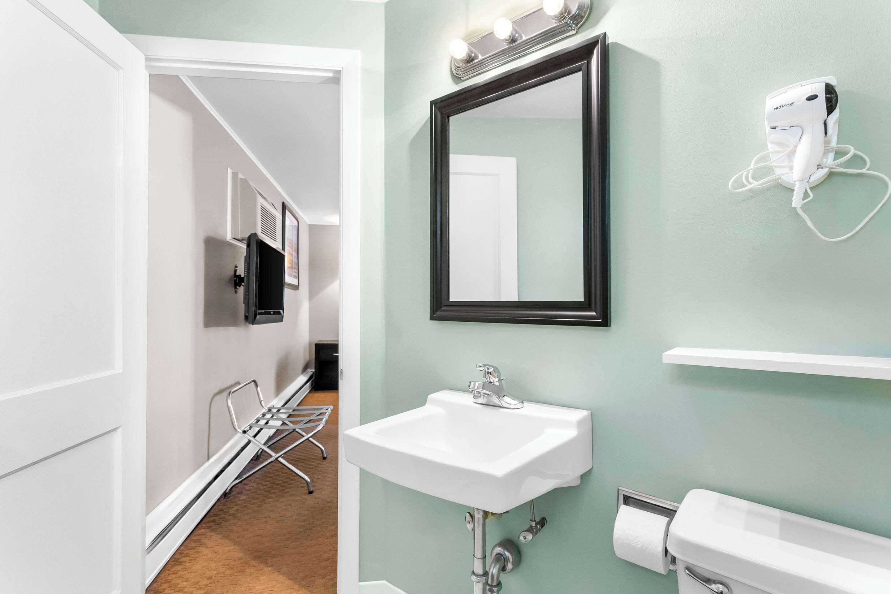 A bathroom with a white sink, a mirror, and a hairdryer mounted on the wall.
