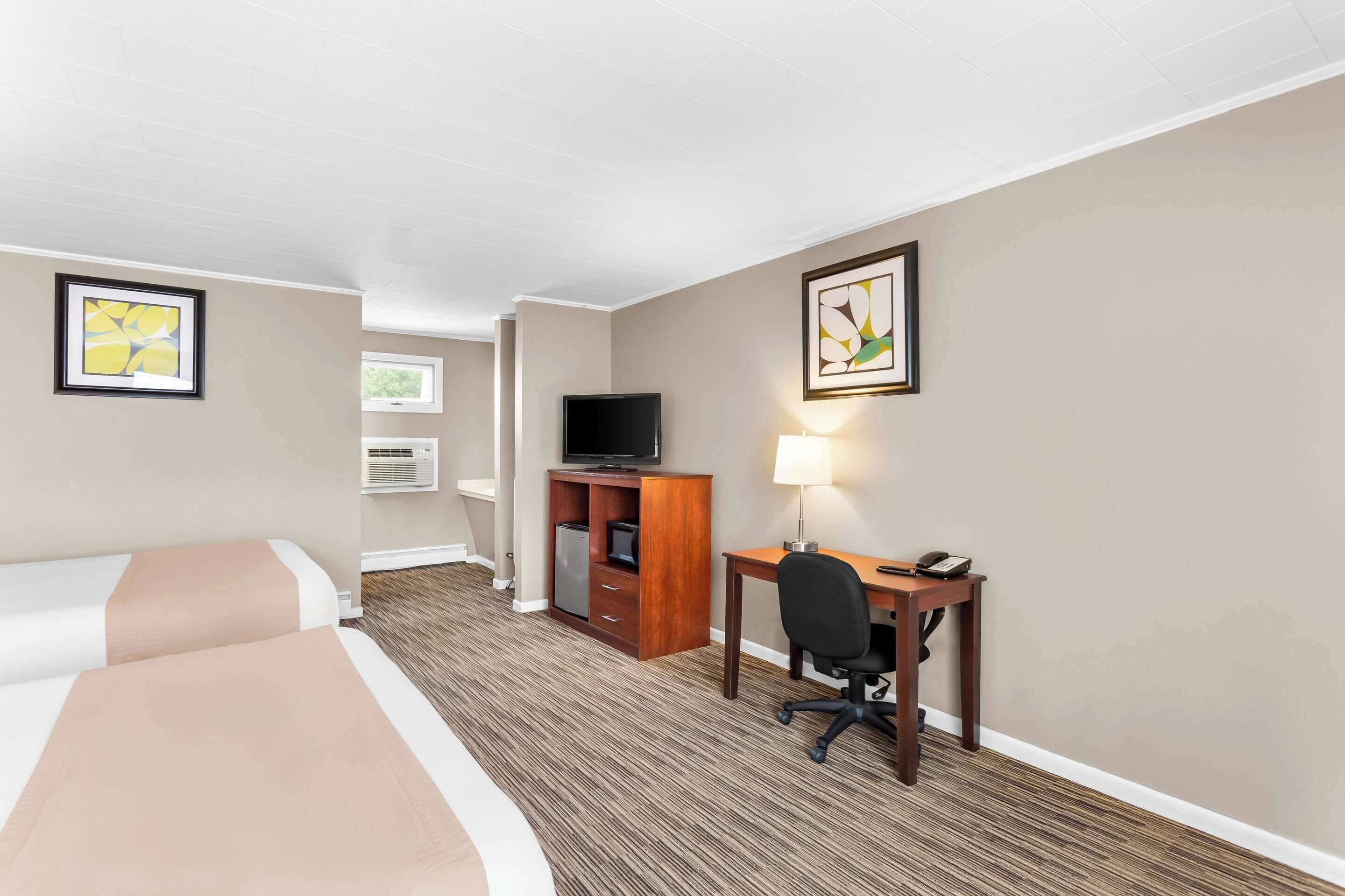 Habitación de hotel con cama, escritorio, silla, televisor y obras de arte en las paredes.