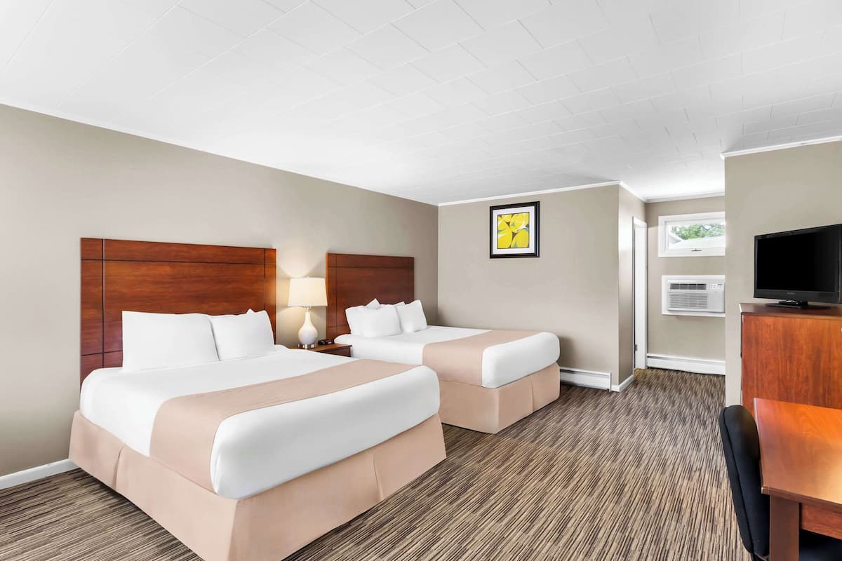 A hotel room with two beds, a desk, a TV, and a window.