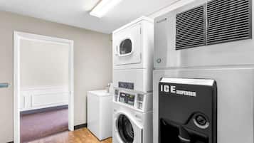 A laundry room with a front-loading washer and dryer, a wall-mounted ice dispenser, and a door leading to another room.