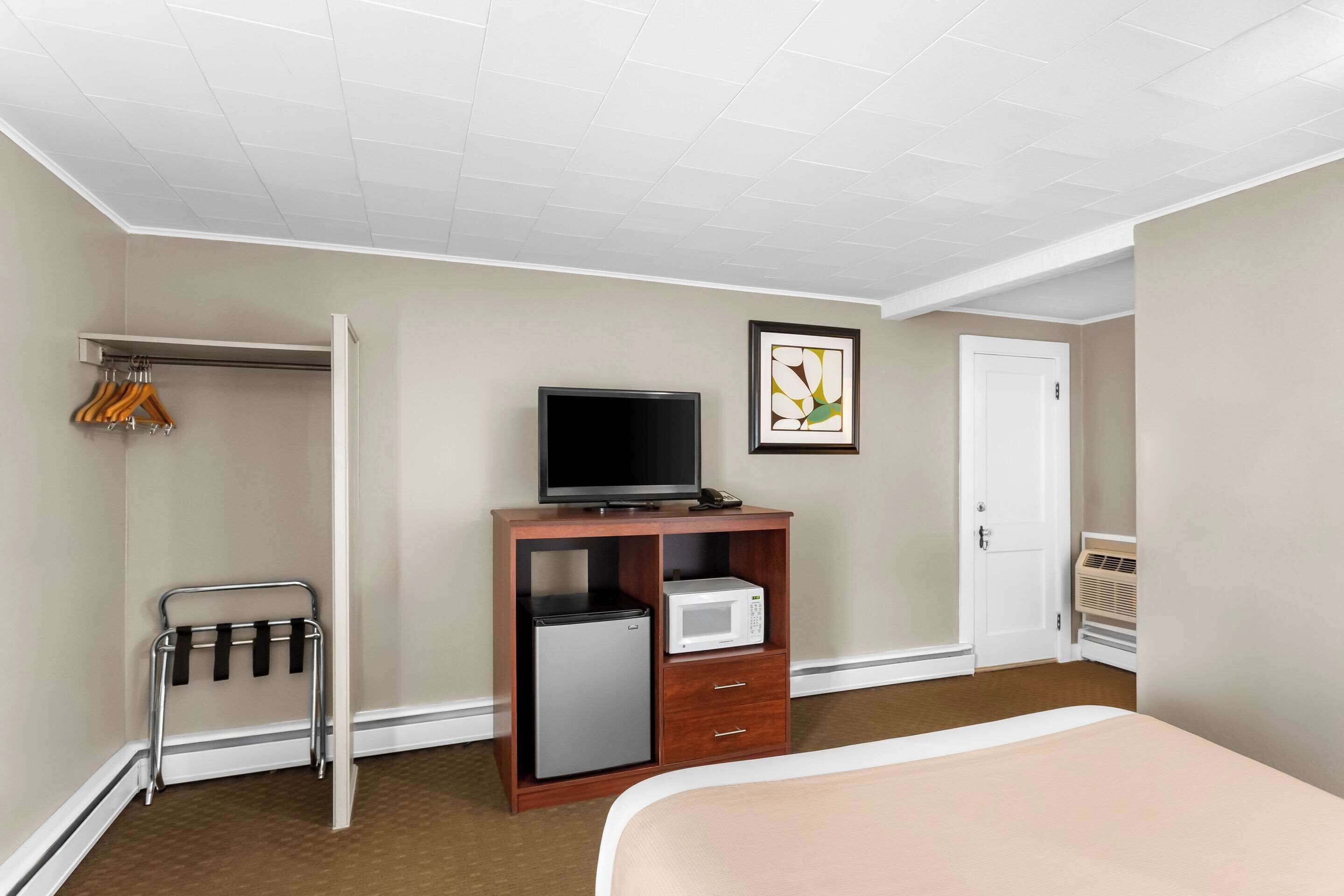 A hotel room with a bed, a TV, a mini-fridge, a microwave, and a coat rack.