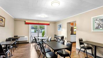 Un salón de conferencias con mesas y sillas, una puerta con cortina roja y beige, y un cuadro en la pared.