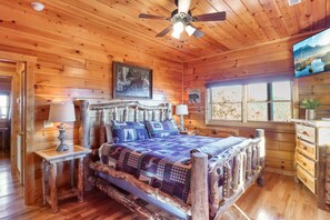 A wooden cabin bedroom with a bed, a ceiling fan, a mounted TV, and a window with a view of the outdoors. - Panoramic View - Suite 4: Poker Table - Spectacular Mountain Backdrop (sevierville)