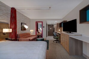 Habitación de hotel con una cama grande, un escritorio con televisión de pantalla plana, una silla y una lámpara de escritorio.