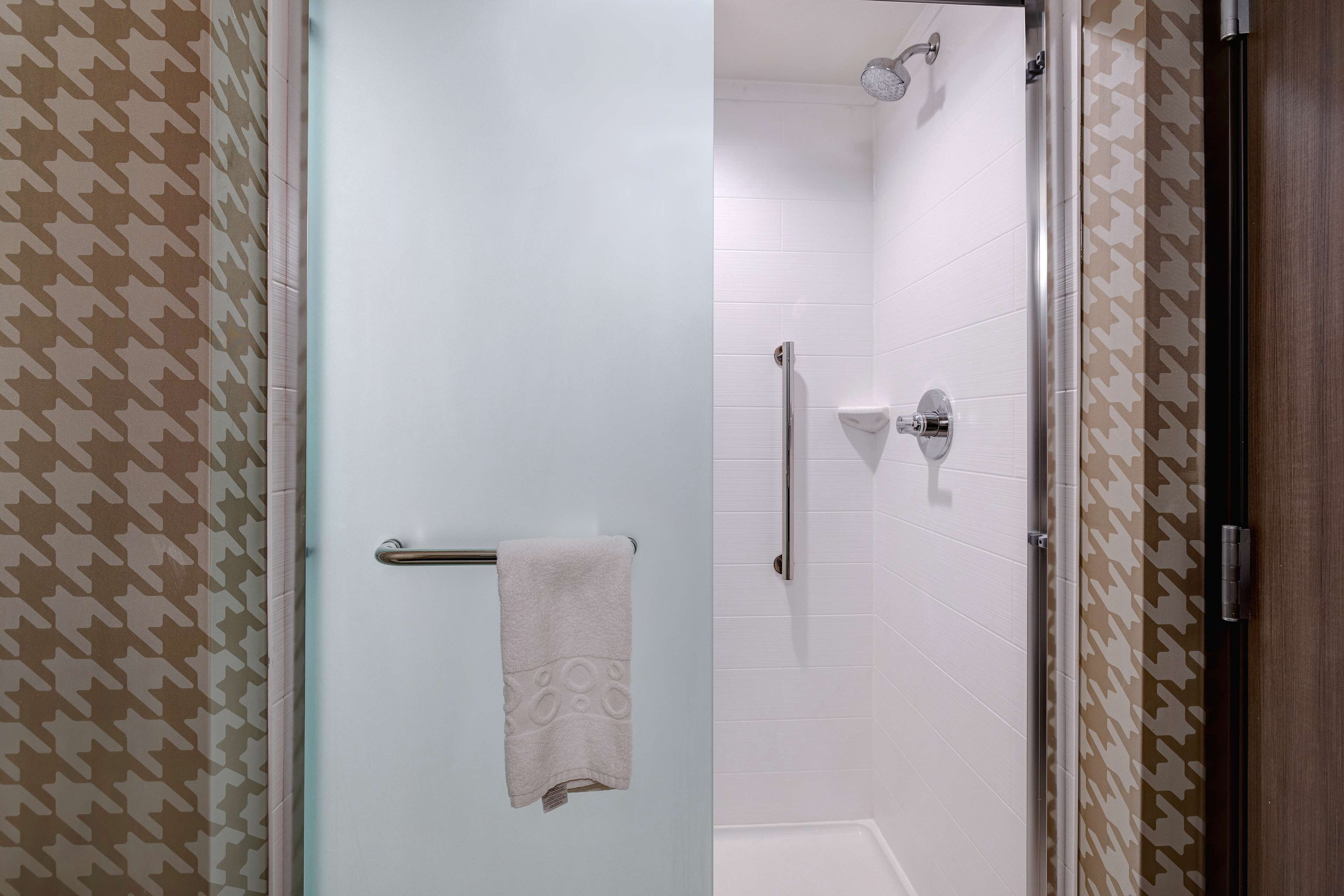 A bathroom with a glass shower door, white tiled walls, and a patterned wall design.