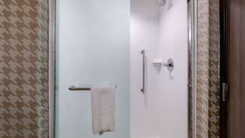 A bathroom with a glass shower door, white tiled walls, and a patterned wall design.