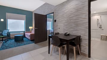 A hotel room with a dining area, a sofa, a chair, a table, and a bathroom visible through an open door.