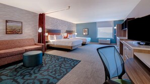 Een hotelkamer met een bank, twee bedden, een bureau, een televisie en een groot raam.
