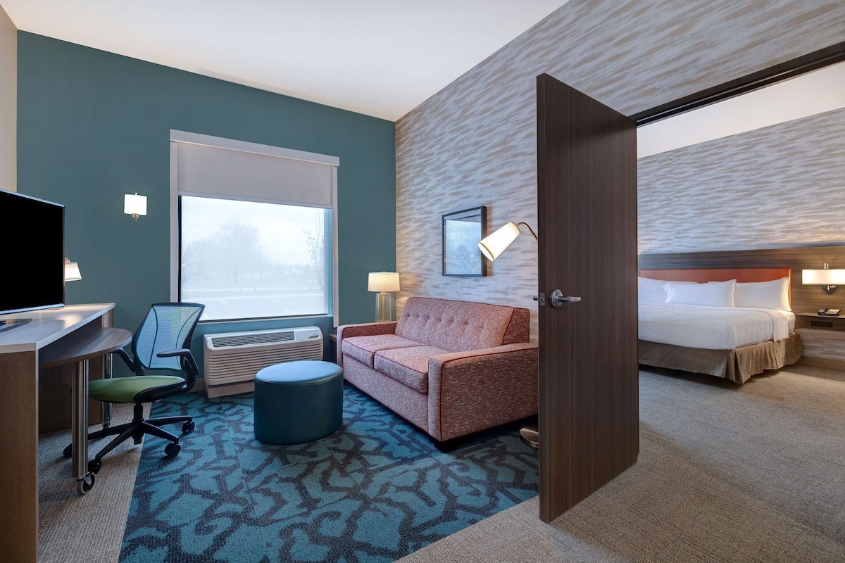 Een hotelkamer met een bed, een slaapbank, een bureau met een computer, een stoel, een lamp en een raam.