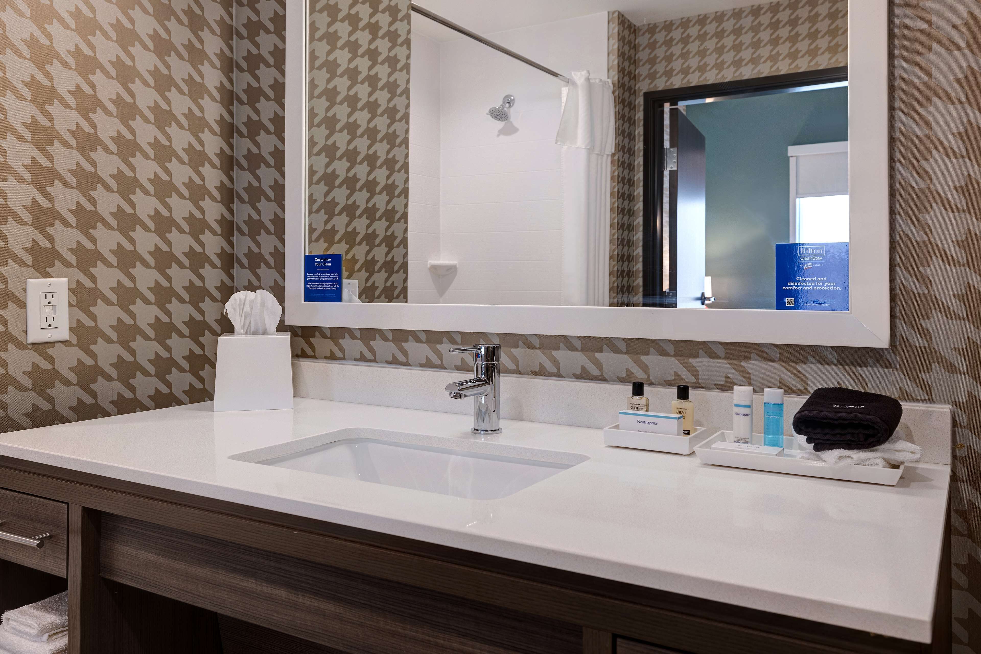 A hotel bathroom with a white sink, a mirror, toiletries, and a towel rack.
