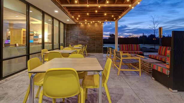 Een terras buiten met gele stoelen en tafels, een houten pergola met lichtjes, en uitzicht op de lucht.