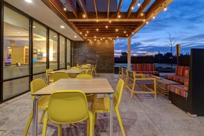An outdoor patio with yellow chairs and tables, a wooden pergola with string lights, and a view of the sky. - Home2 Suites by Hilton Dekalb (DeKalb)