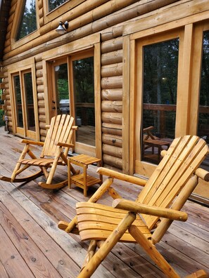 A wooden log cabin with a deck featuring rocking chairs and a small table.