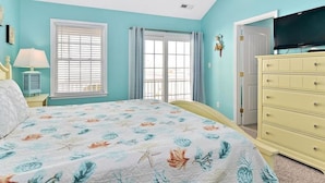 A bedroom with a bed, a dresser, a television, and two windows with curtains.