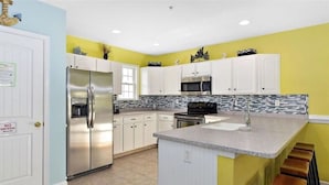 A modern kitchen with white cabinets, a stainless steel refrigerator, a microwave, and a granite countertop.
