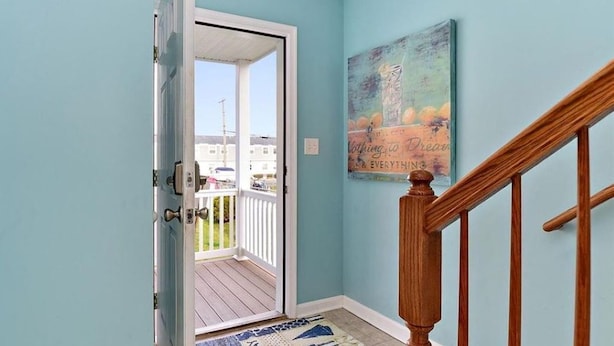 A hallway with light blue walls, a wooden staircase, and a door leading to a balcony.