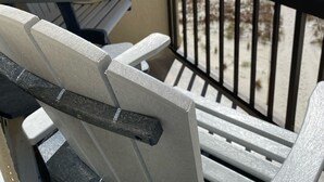 Ein Balkon mit Meerblick, ausgestattet mit zwei Adirondack-Stühlen und einem schwarzen Metallgeländer.