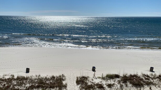 Ein Strand mit freiem Blick auf das Meer, ein sandiger Weg zum Wasser und ein Wegweiser in der Mitte.
