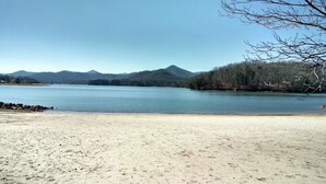A beach with a sandy shore, a calm lake, and a forested mountain range in the background. - Riverfront cabin, arcade, hot tub, pool, trout fishing, pet friendly (Hiawassee)
