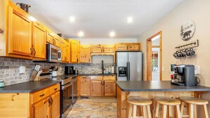 A kitchen with wooden cabinets, a refrigerator, a microwave, and a coffee maker. - Riverfront cabin, arcade, hot tub, pool, trout fishing, pet friendly (Hiawassee)